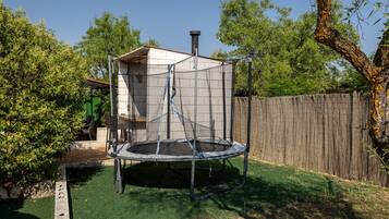 A trampoline in a backyard with a wooden fence, a tree, and a shed.