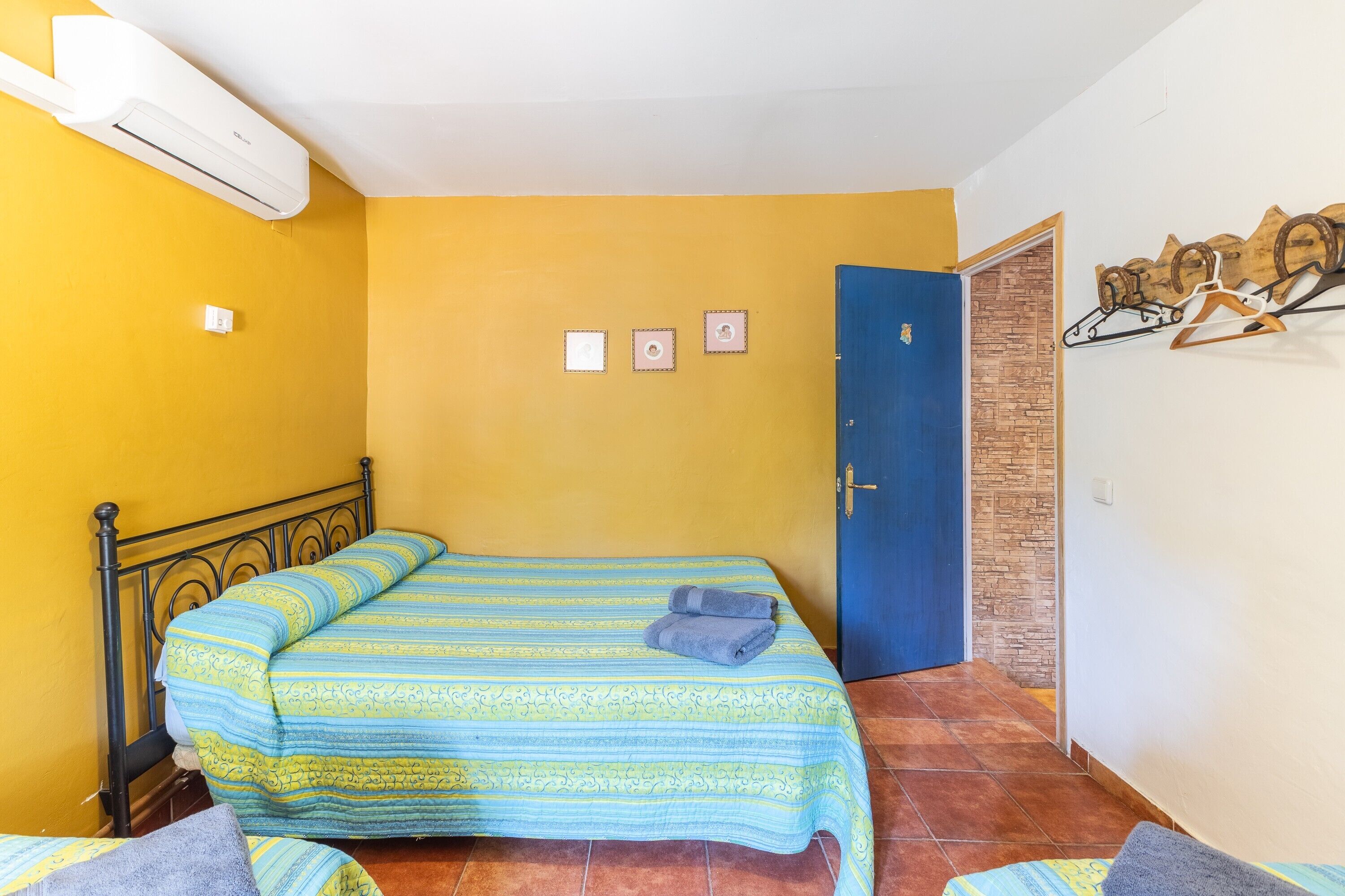 A room with a bed, a blue door, a wall-mounted air conditioner, and a wall with three small pictures.