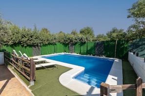 A rectangular swimming pool with a blue interior, surrounded by a white deck and a wooden fence.