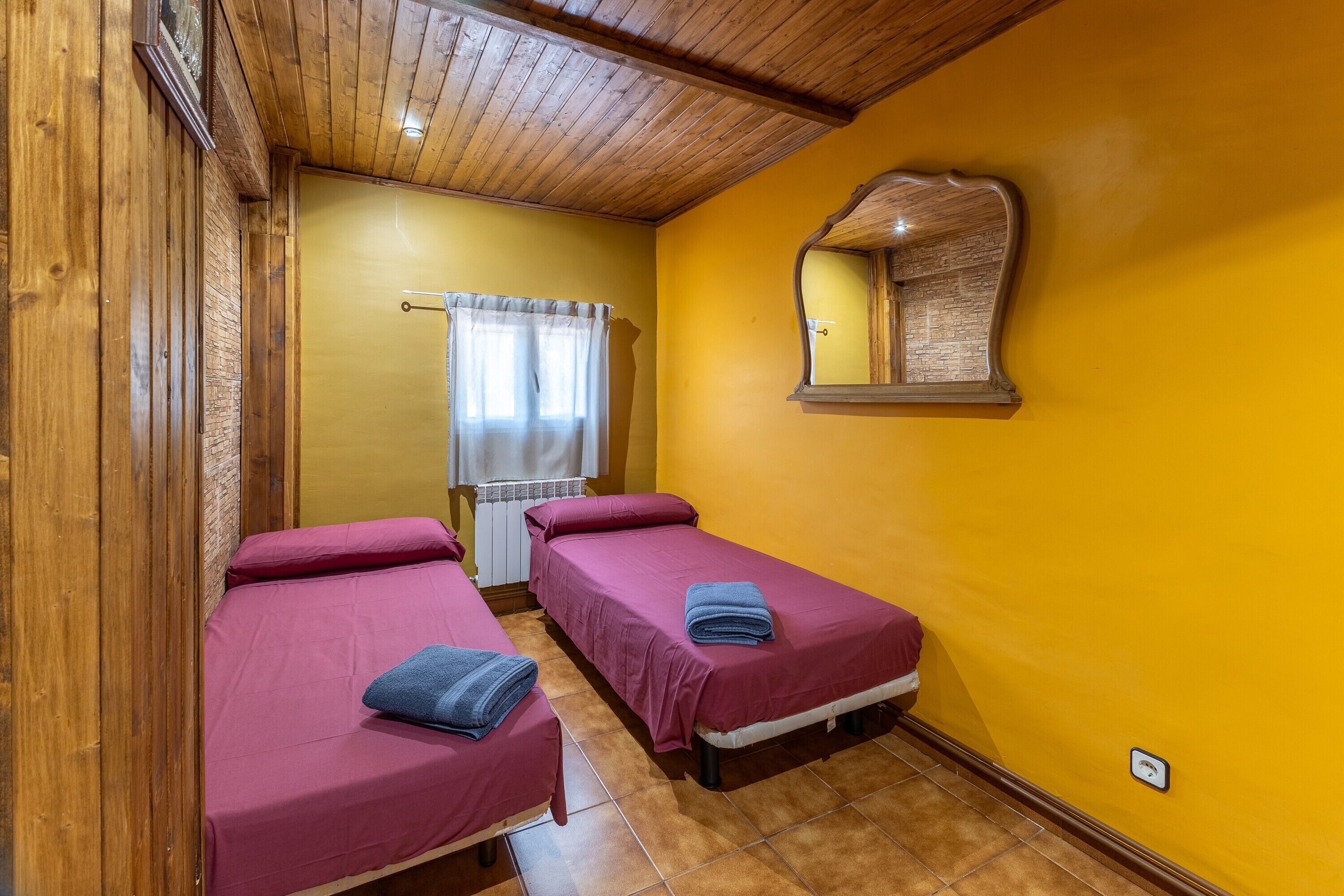 Ein Zimmer mit zwei Betten, Holzwänden, einer gelben Wand, einem Spiegel und einem Fenster mit Vorhängen.