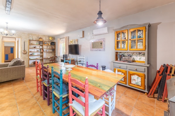 A dining area with a wooden table and colorful chairs, a television, and a kitchen area with cabinets and a stove.