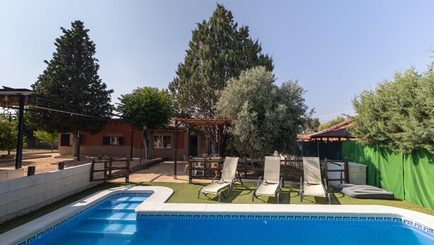 Una piscina con sillones de descanso, una pérgola y una zona de patio techada.