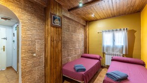 Una habitación con dos camas, paredes de madera, un radiador y una ventana con cortinas.
