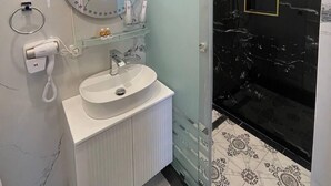 A modern bathroom with a white sink, a round mirror, and a glass-enclosed shower. - ARDANI Hotel  (Samarkand)