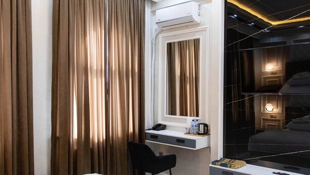 A hotel room with a bed, a desk with a chair, a large mirror, and a wardrobe. - ARDANI Hotel  (Samarkand)