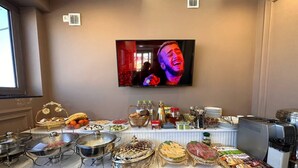 A buffet setup with various food items and a television mounted on the wall. - ARDANI Hotel  (Samarkand)