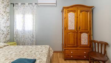 A bedroom with a bed, a wooden wardrobe, a chair, and a window with floral curtains.