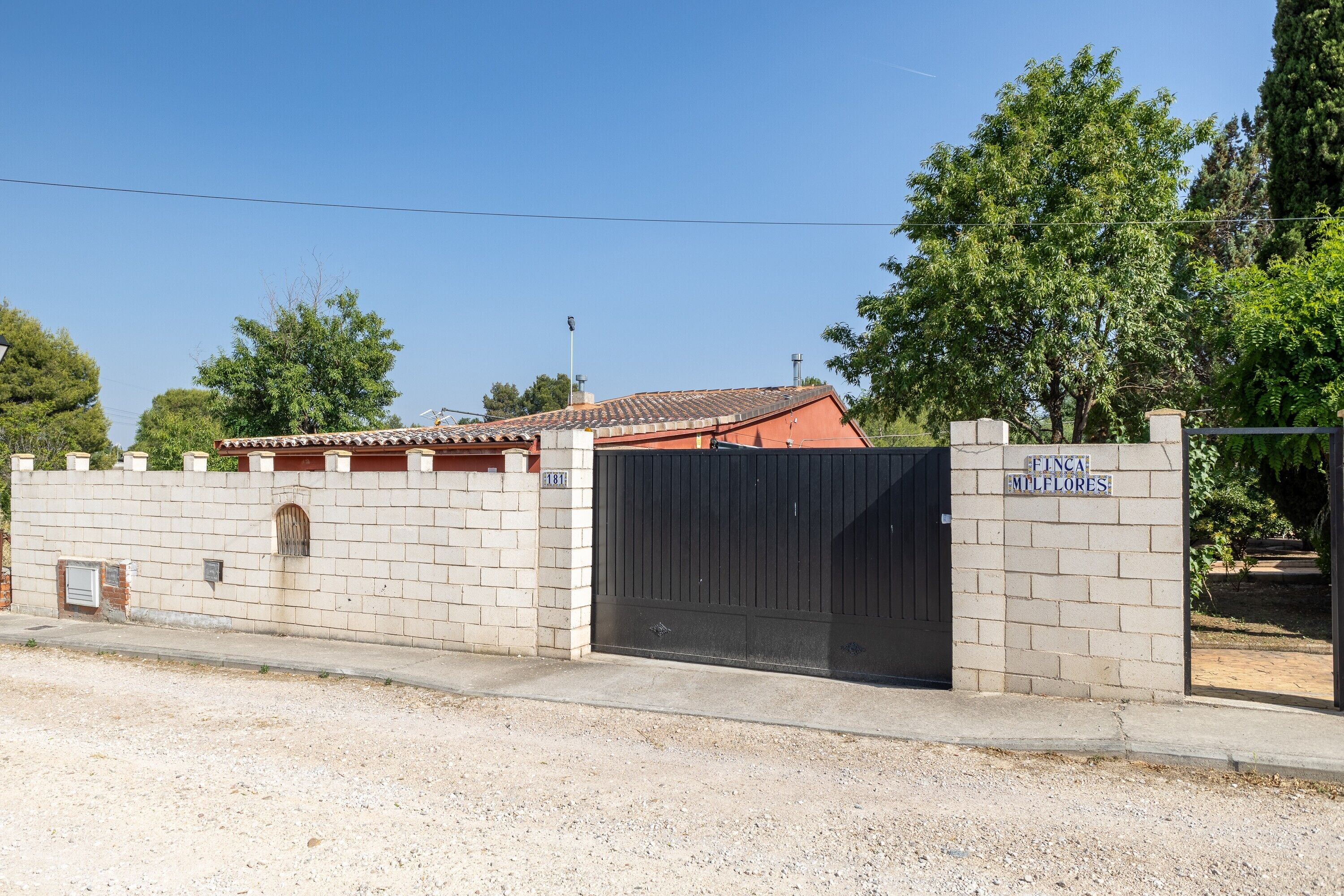 Propiedad amurallada con muro de ladrillo, portón metálico y un letrero que dice 'FINCA MTLFLORES'.