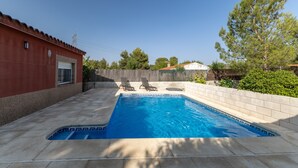 Una piscina amb dues gandules, un edifici vermell i un arbre.