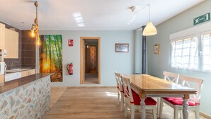 Una cuina moderna amb una illa de pedra, taula de dinar de fusta i cadires. Hi ha un extintor de foc a la paret i una porta que condueix a una altra habitació.