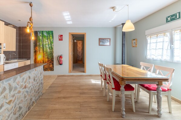 Eine moderne Küche mit einer Steininsele, einem Holzes Esstisch und Stühlen. An der Wand hängt ein Feuerlöscher, und eine Tür führt in einen anderen Raum.