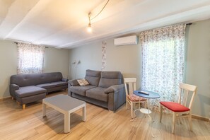 A living room with a grey sofa, a small table, a red chair, and a round table with a remote control.
