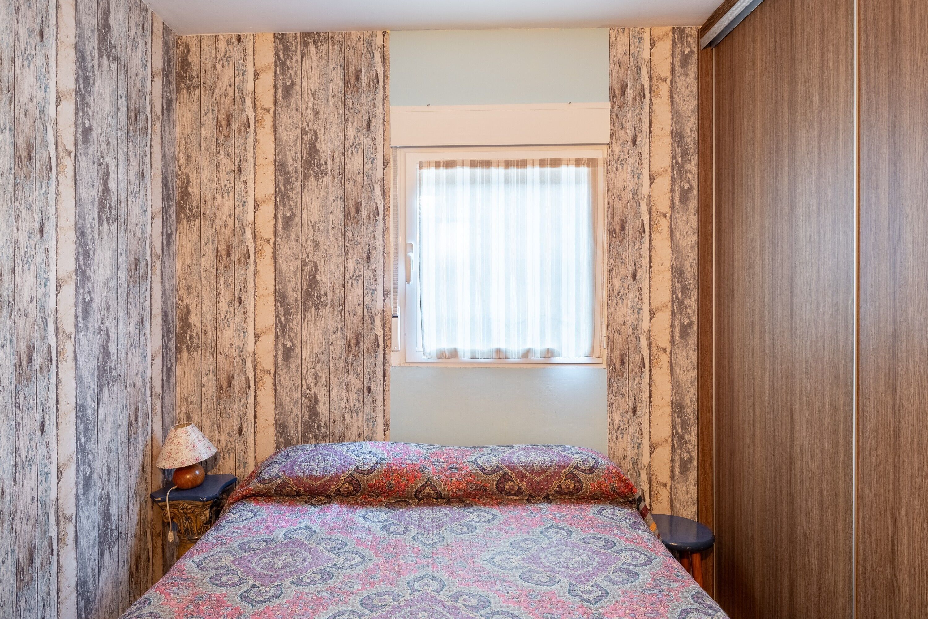 A room with a bed, a window with curtains, a lamp, and a small table.