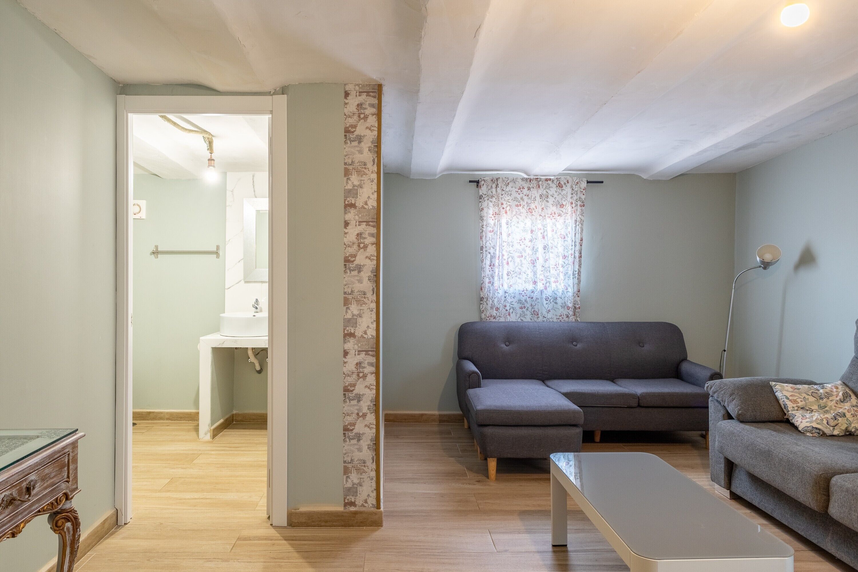Una sala de estar con un sofá gris, una mesa de centro de madera y un pilar con diseño.