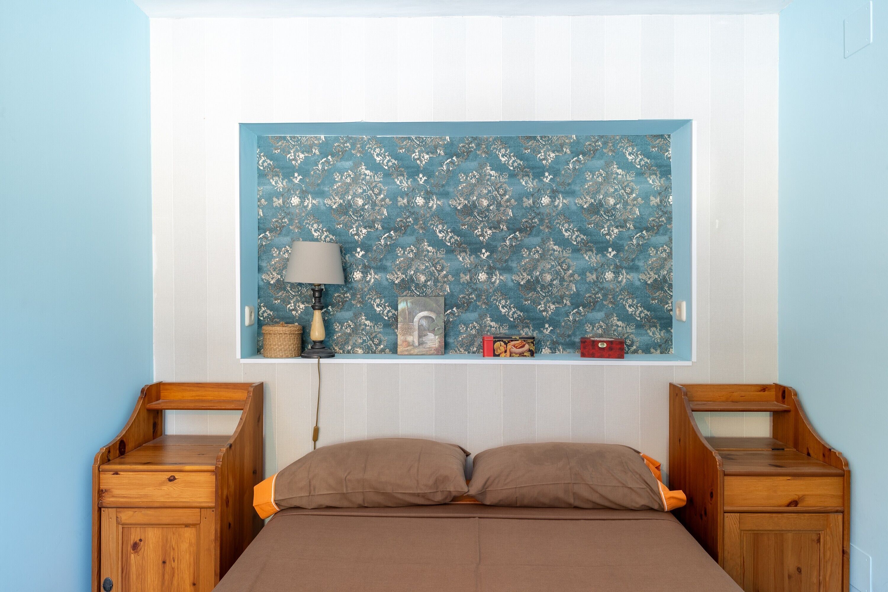 Un dormitorio con una cama, dos mesitas de noche de madera, una lámpara y un panel decorativo en la pared.