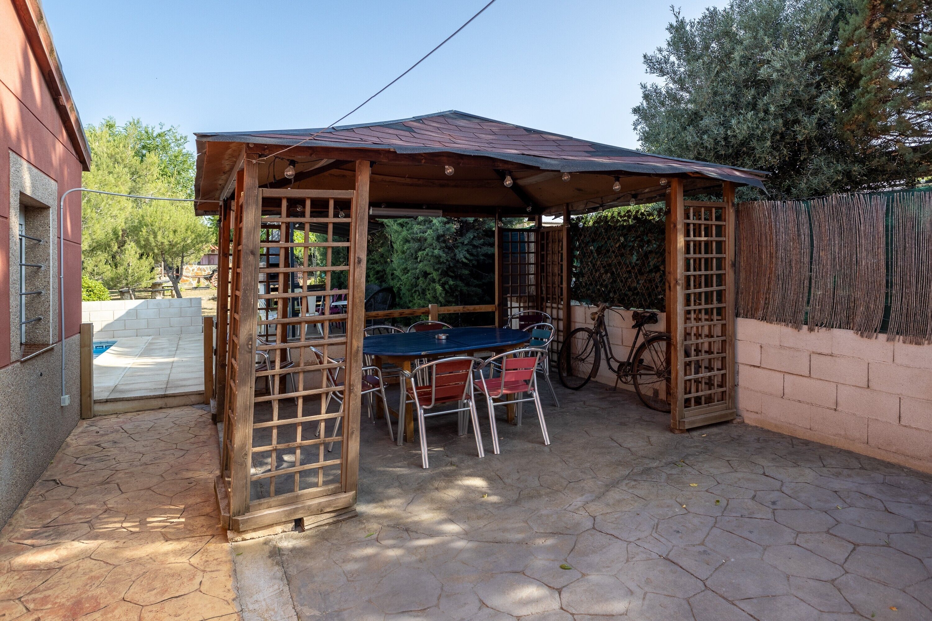 Un espacio cubierto para sentarse al aire libre, con una mesa, sillas, una bicicleta y una valla de madera.