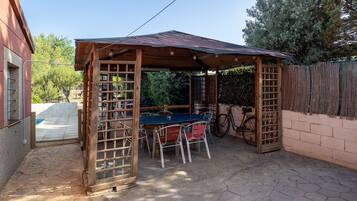 Un espacio cubierto para sentarse al aire libre, con una mesa, sillas, una bicicleta y una valla de madera.