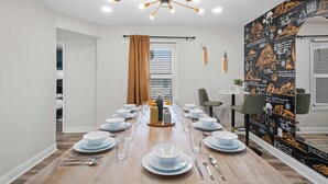 A dining area with a long table set for a meal, a chandelier, and a blackboard wall with chalk drawings. - Adventure Basecamp, Walks to Kaymoor and Long point Trails, Hot Tub & Game Room (Fayetteville)