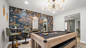 A pool table with a black cloth, two green barstools, and a wall with a black and gold travel-themed mural. - Adventure Basecamp, Walks to Kaymoor and Long point Trails, Hot Tub & Game Room (Fayetteville)