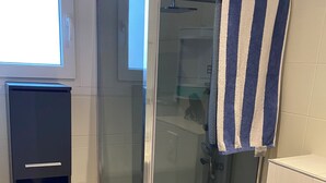 Une salle de bain moderne avec une douche à parois de verre, un meuble noir contenant des serviettes et une serviette rayée accrochée au mur.
