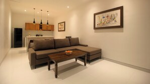 A modern living room with a sectional sofa, a wooden coffee table, pendant lights, and a kitchen area in the background. - Bougainvillea Villas Cemagi by Parigata (Cemagi)