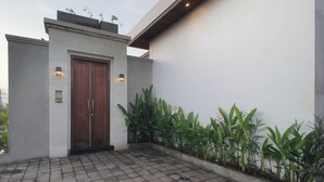 A modern building with a wooden door, a white wall, and a tiled patio area with plants. - Bougainvillea Villas Cemagi by Parigata (Cemagi)