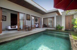 Uma área de piscina moderna ao ar livre, com espaço para sentar, mesa de jantar e um grande guarda-sol.