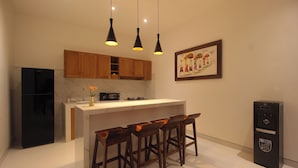 A modern kitchen with wooden cabinets, a black refrigerator, a marble countertop, and bar stools. - Bougainvillea Villas Cemagi by Parigata (Cemagi)