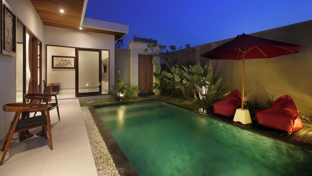 A modern outdoor pool area with a wooden deck, seating, and a red umbrella. - Bougainvillea Villas Cemagi by Parigata (Cemagi)