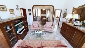 A living room with a sofa, armchairs, a coffee table, and a TV. There is a dining area with a table and chairs visible through a doorway. - La Terrazza sul Borgo (Capoliveri)