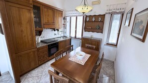 A kitchen with wooden cabinets, a dining table with chairs, a stove, and a chandelier. - La Terrazza sul Borgo (Capoliveri)