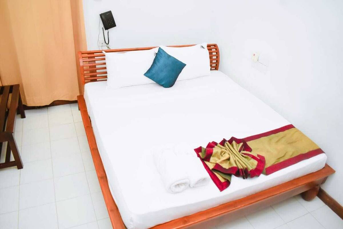 A neatly made bed with a white mattress, a blue pillow, and a red and beige blanket.