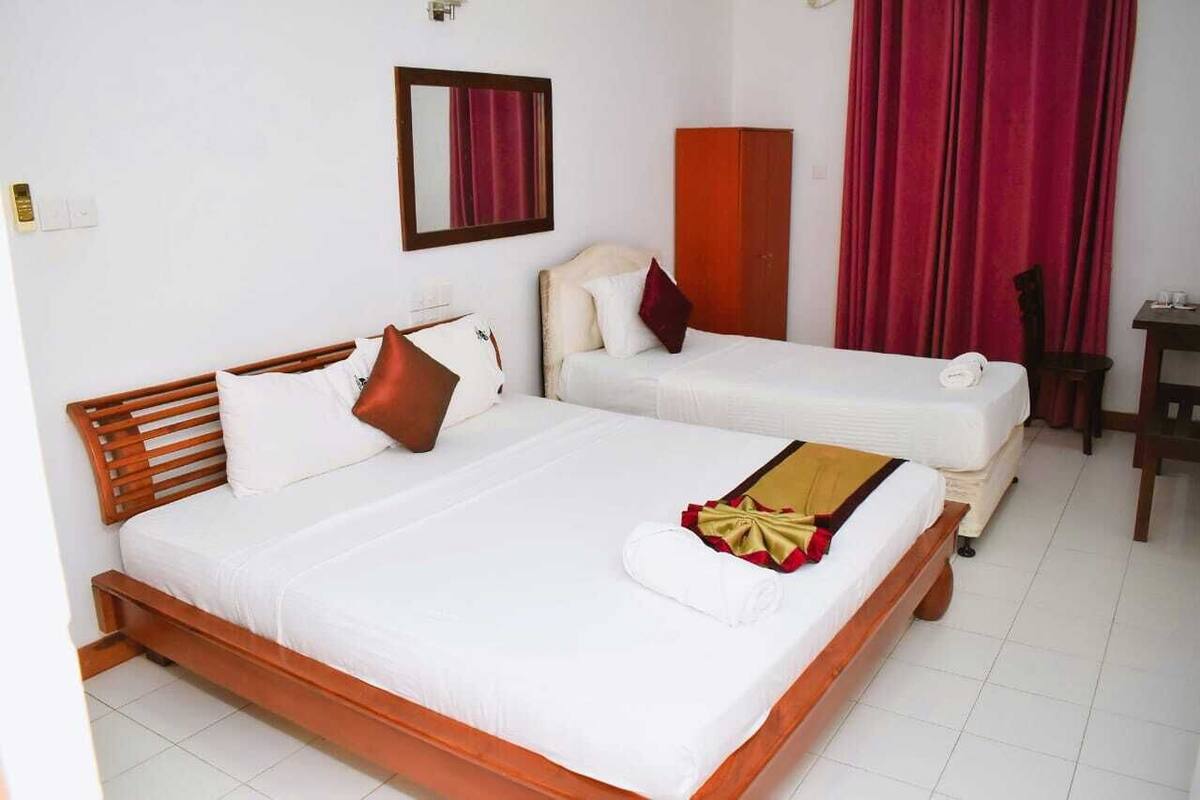 A hotel room with two single beds, a wooden headboard, a mirror, a red curtain, and a desk with a chair.