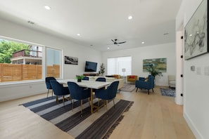 Un soggiorno moderno con zona pranzo, ampie finestre e ventilatore a soffitto.