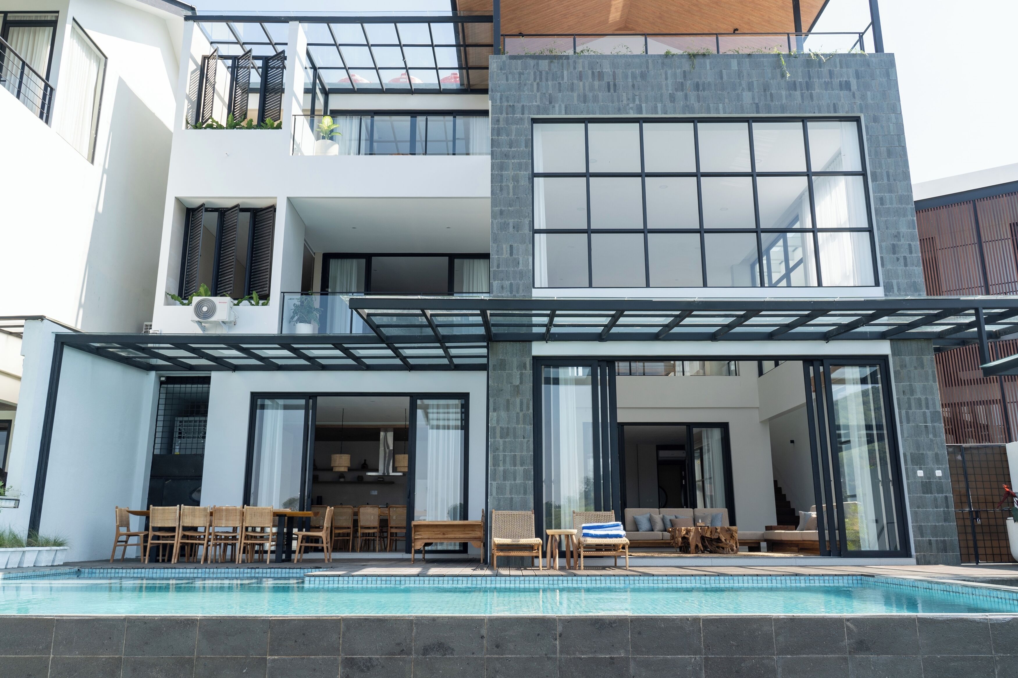 A modern two-story house with a swimming pool, outdoor seating, and large windows.