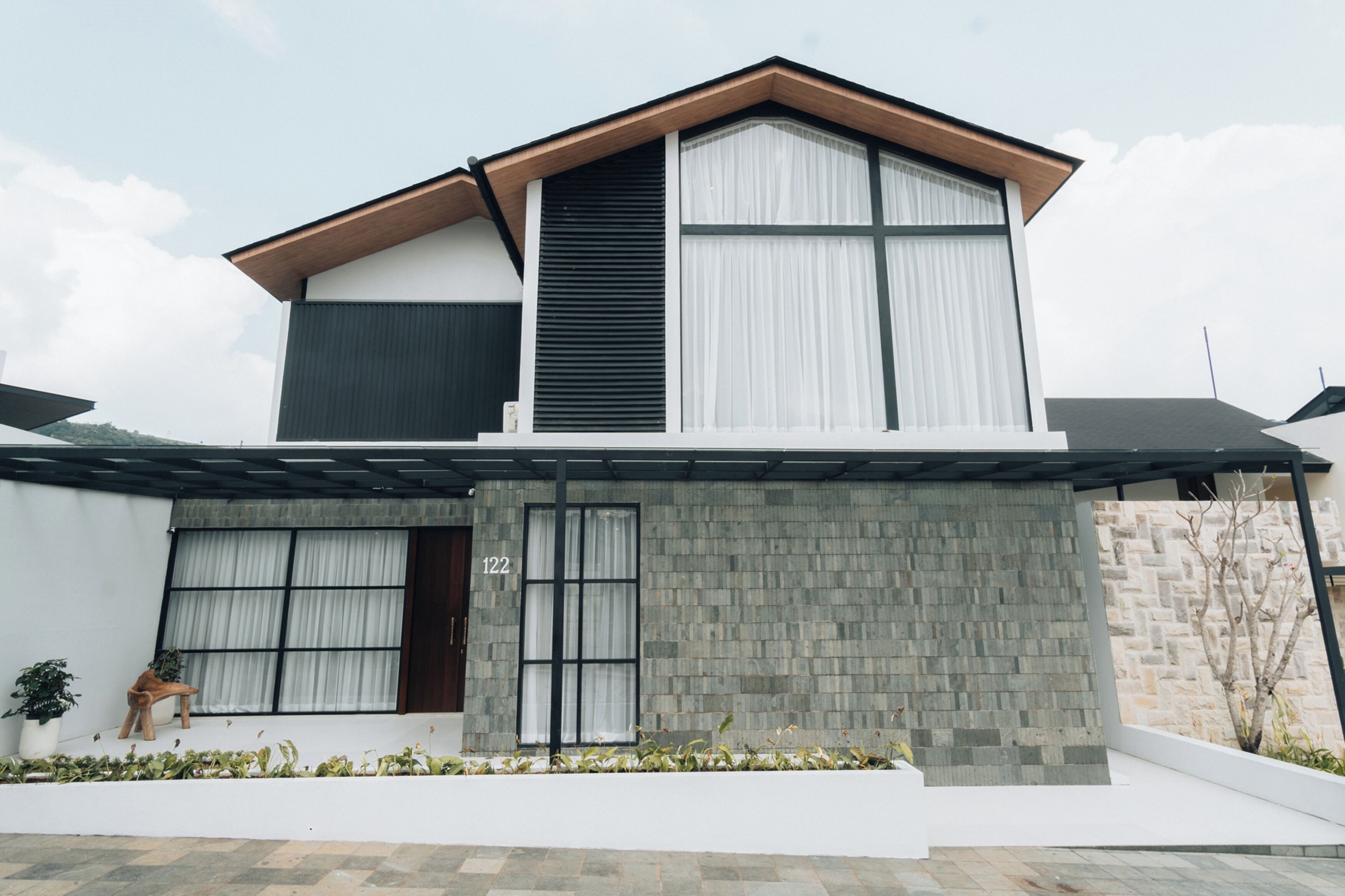 A modern two-story house with a flat roof, large windows, and a stone facade.