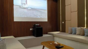 Una sala de estar moderna con un televisor de pantalla plana grande montado en una pared de madera, un altavoz negro pequeño, una mesa de centro de madera y un sofá beige con cojines.