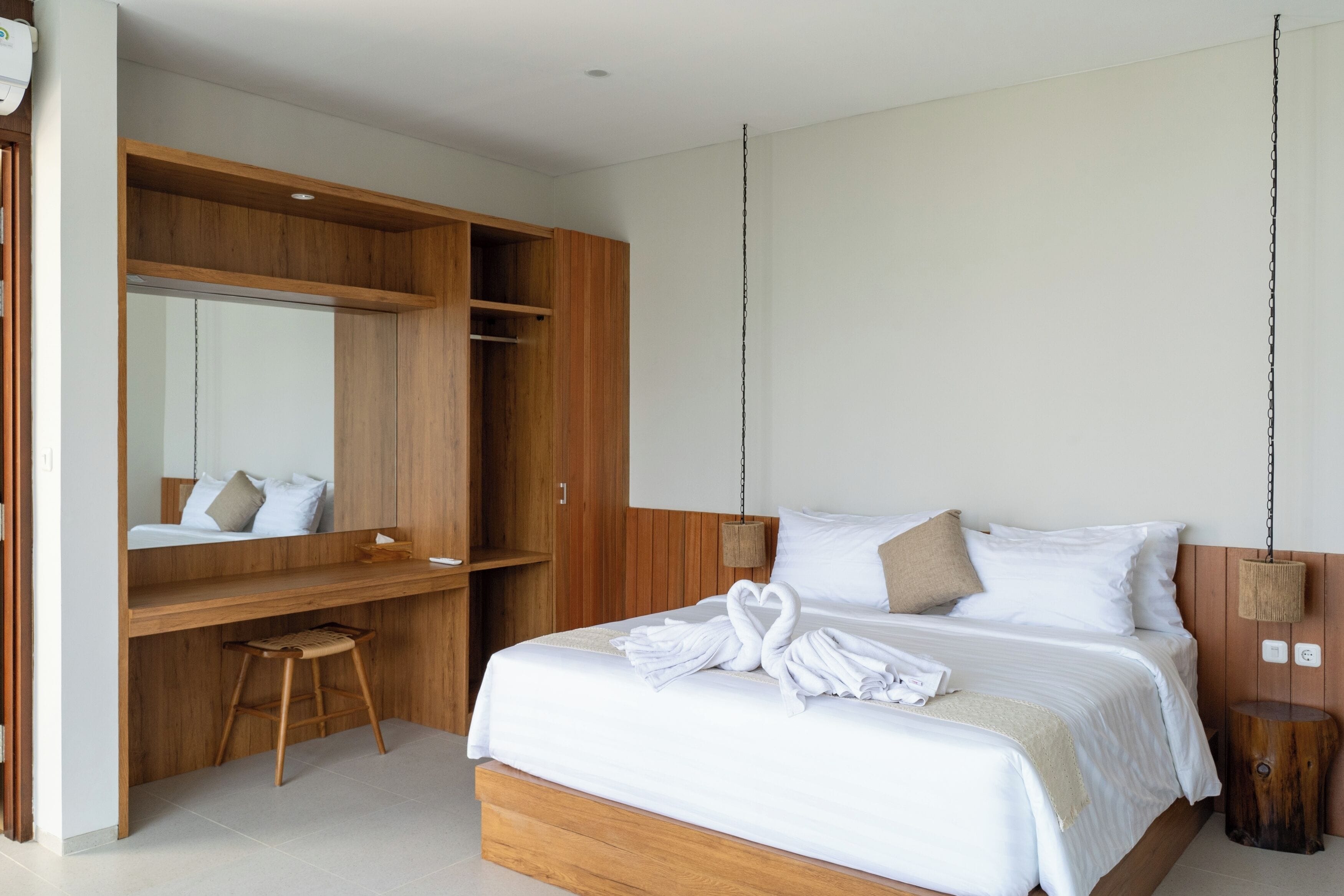 Un dormitorio moderno con un escritorio de madera, una cama grande con ropa blanca y una lámpara colgante.