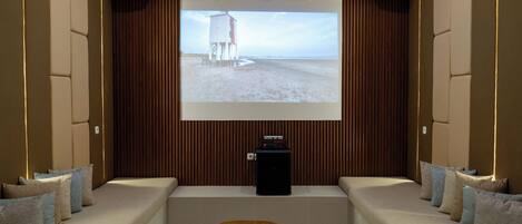 Un cine en casa con pantalla grande, asientos cómodos y una mesa de centro.