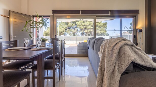 Un salon moderne avec un canapé, une table à manger et des chaises. Il y a une grande fenêtre donnant sur des arbres et un balcon.