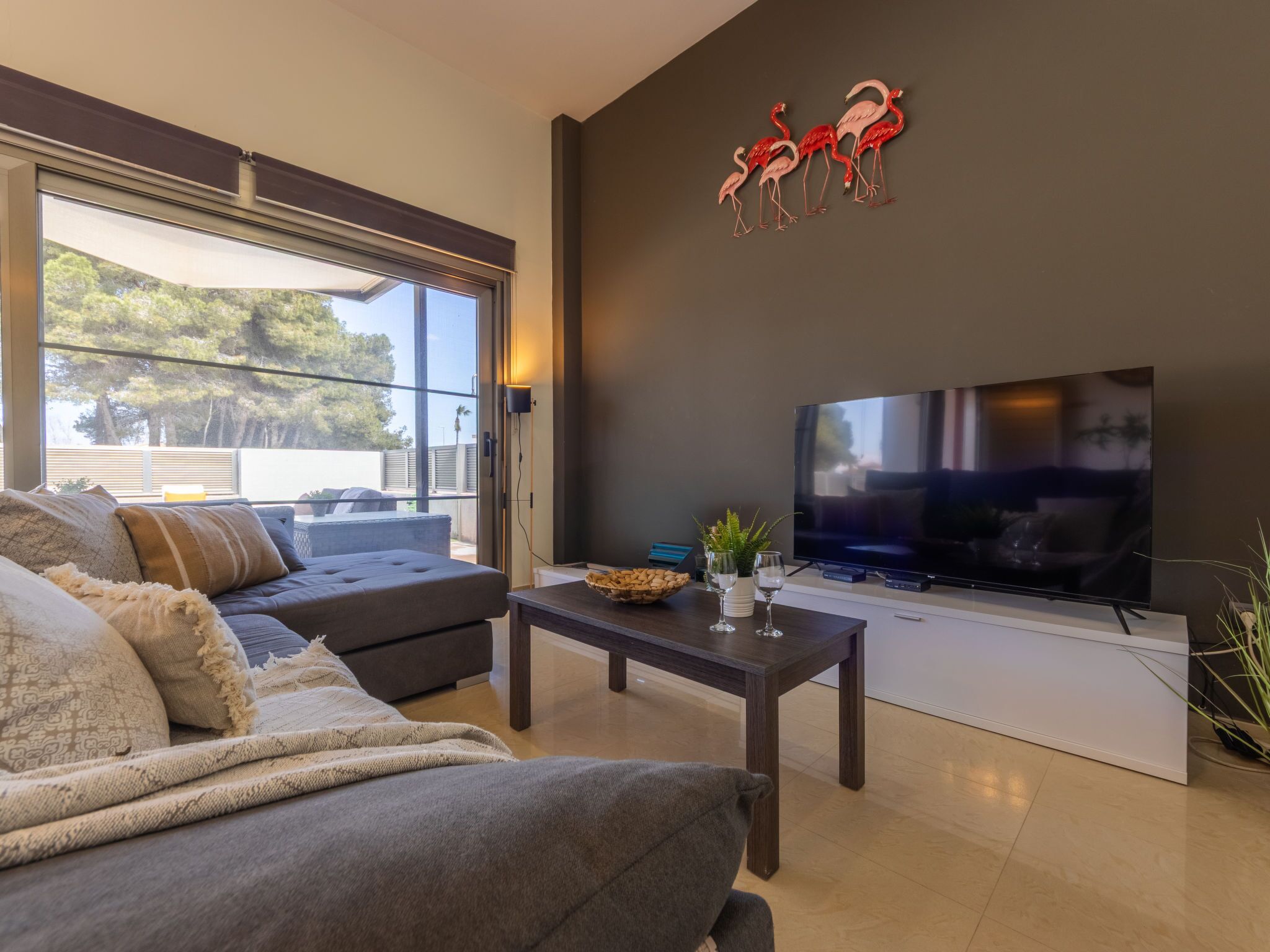 A modern living room with a large flat-screen TV, a dark sofa, and a coffee table with decorative items.