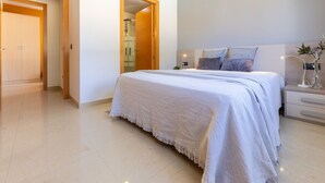 Une chambre moderne avec un grand lit, des tables de chevet, une commode, une lampe fixée au mur et une porte donnant sur une autre pièce.
