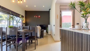 Une cuisine moderne avec un coin repas, comprenant un mur de couleur sombre, une table à manger en bois avec des chaises, et un îlot de cuisine agrémenté d’un vase en verre.