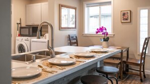 Una cucina moderna con un'isola centrale, un'area pranzo con tavolo e sedie, e vista all'esterno da una finestra.