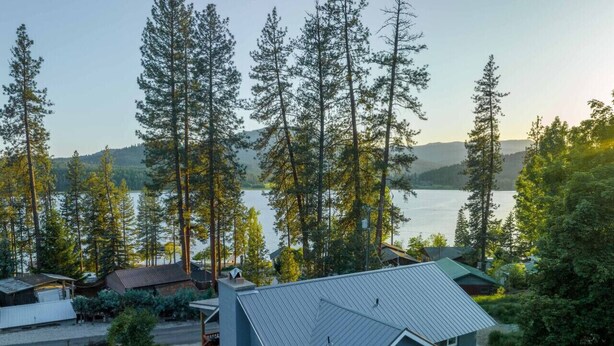 Una piccola casa con tetto spiovente, circondata da alberi e da uno specchio d'acqua.