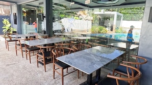 An outdoor dining area with glass tables and wooden chairs, a pool in the background, and a view of the surrounding greenery. - Lucky Tito Diving Inn Coron (Coron)