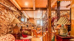 A cozy room with a stone wall, wooden furniture, a red sofa, a wooden dining table, and a red cabinet.