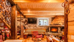 A cozy cabin interior with a stone fireplace, wooden furniture, and a stone wall.