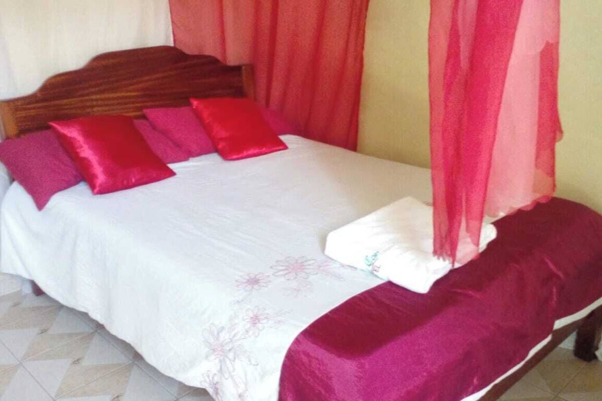 A bed with a wooden headboard, white and pink bedding, and a red canopy.