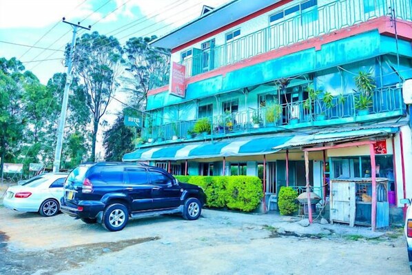 A multi-story hotel with a balcony on the upper floor, a covered front area, and a parked SUV. - Quila Hotel Gilgil (Gilgil)